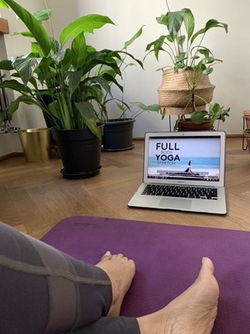 A yoga mat unrolled at home in front of a laptop playing a yoga stretch video