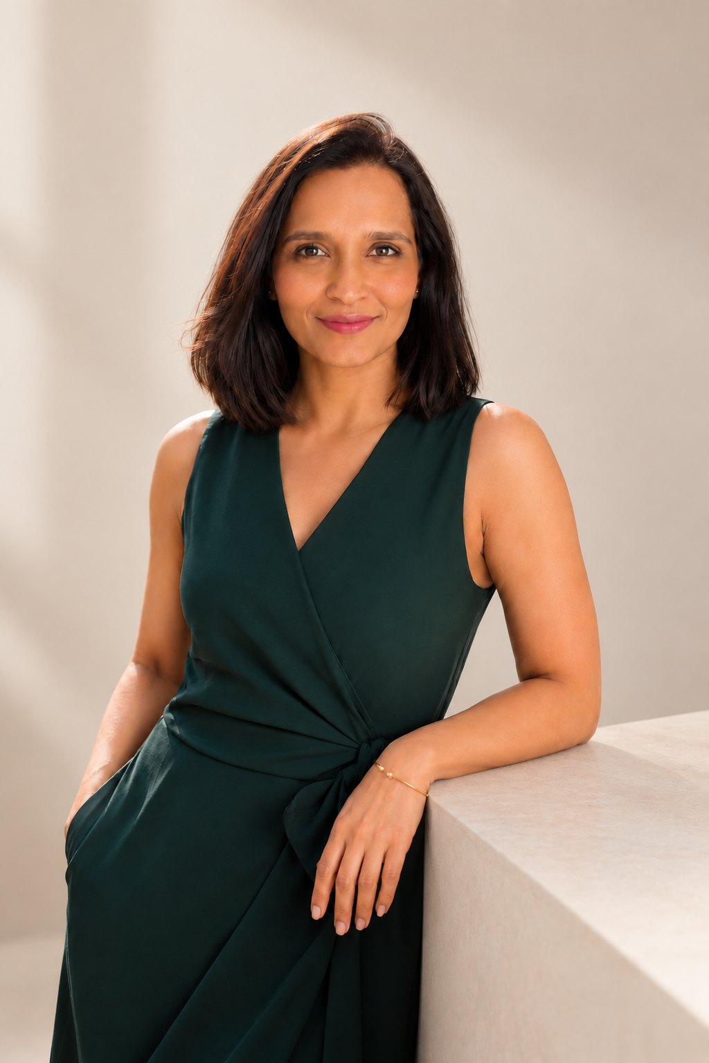 Portrait of Tina Nayak in a green dress, leaning on a plinth in soft daylight